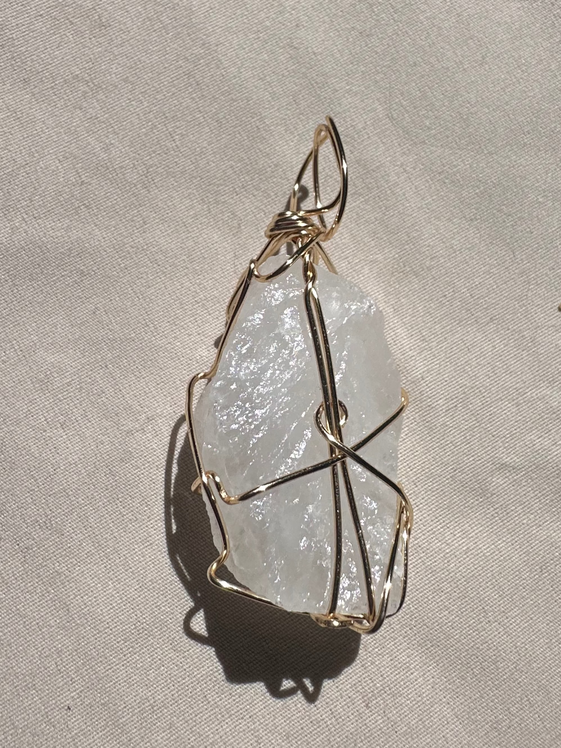 Crystal pendant with gold wire wrapping on a light gray background