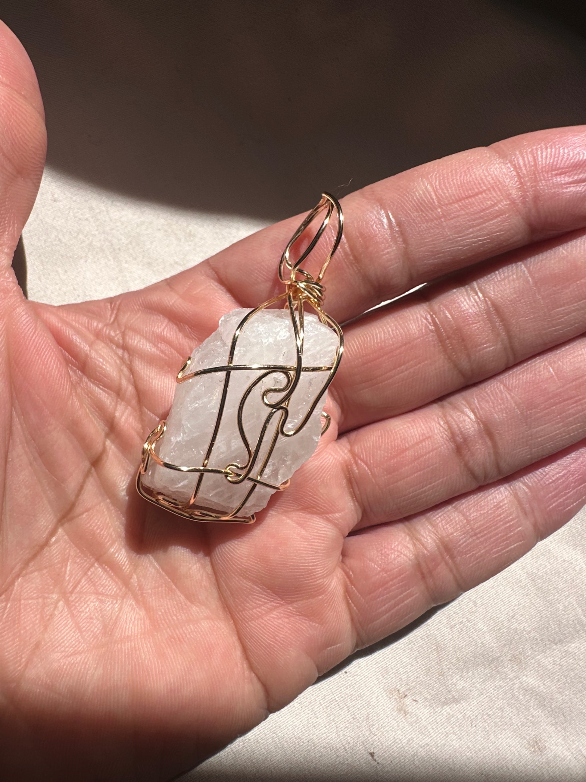 Hand holding a crystal pendant with gold wire wrapping on a neutral background